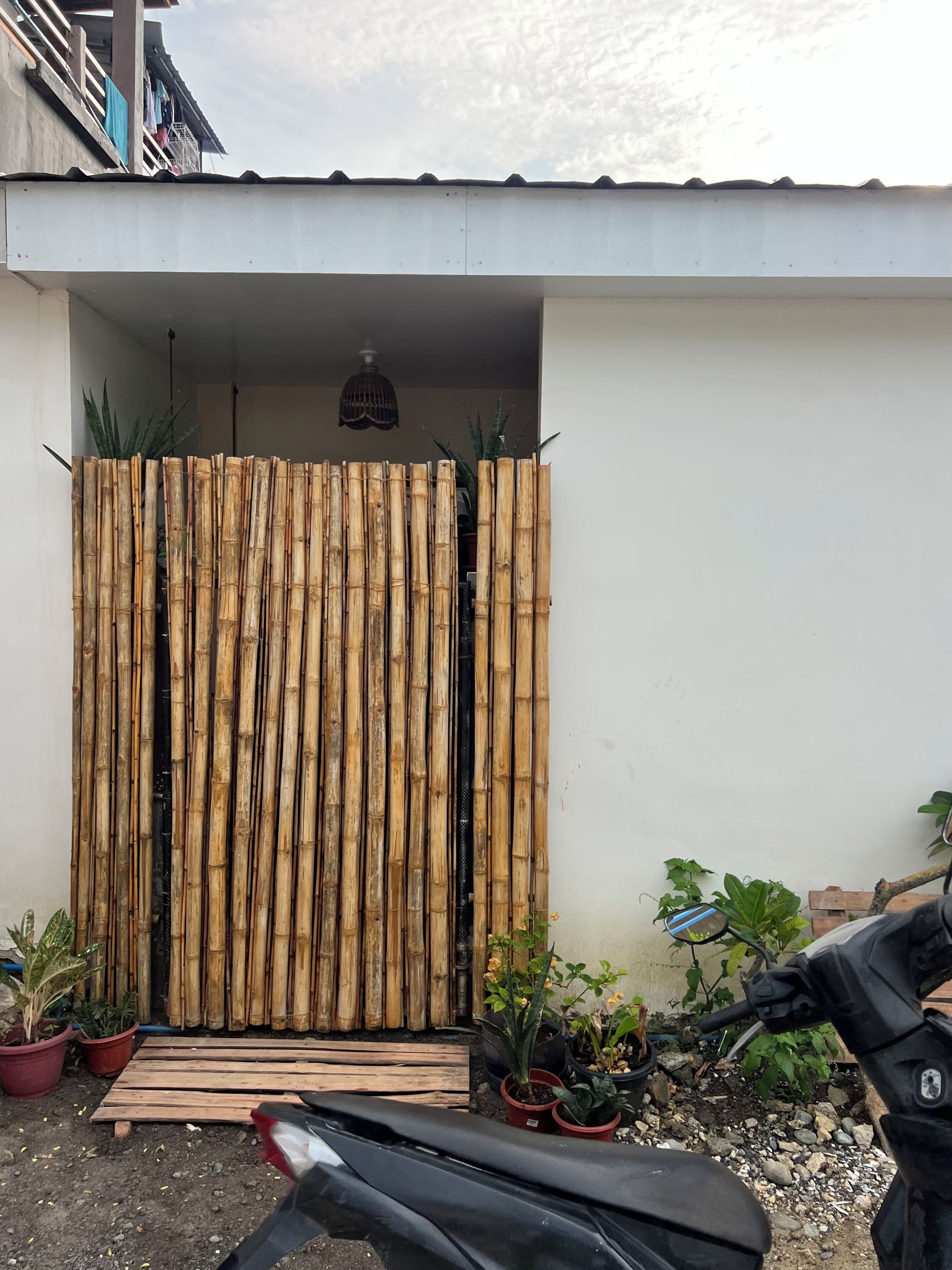A building entrance with a bamboo screen, potted plants, and a motorcycle parked outside.