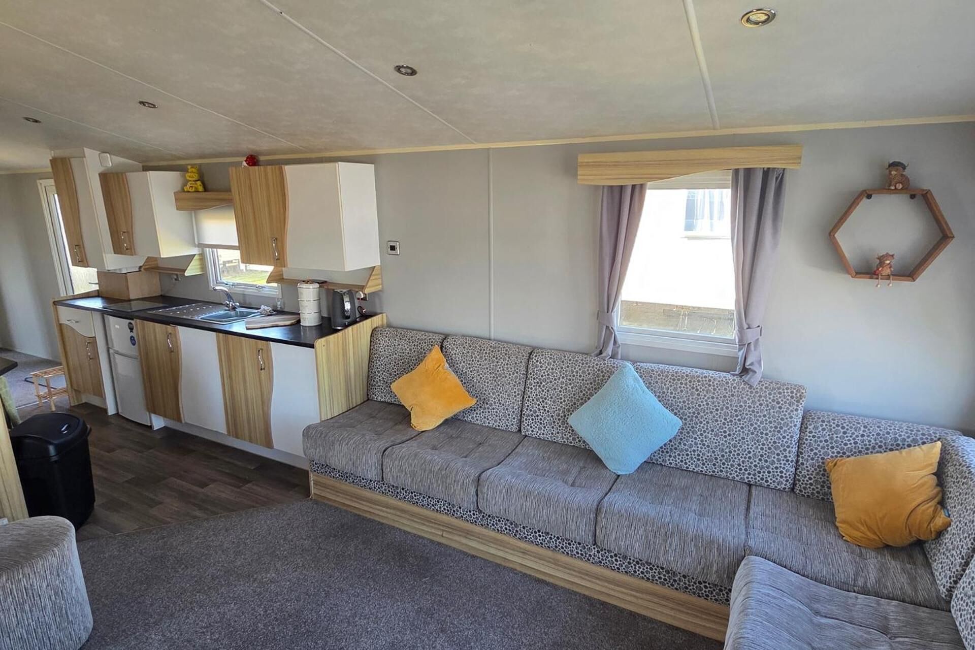 Interior compacto de una caravana con kitchenette, sofá y ventana con cortinas.