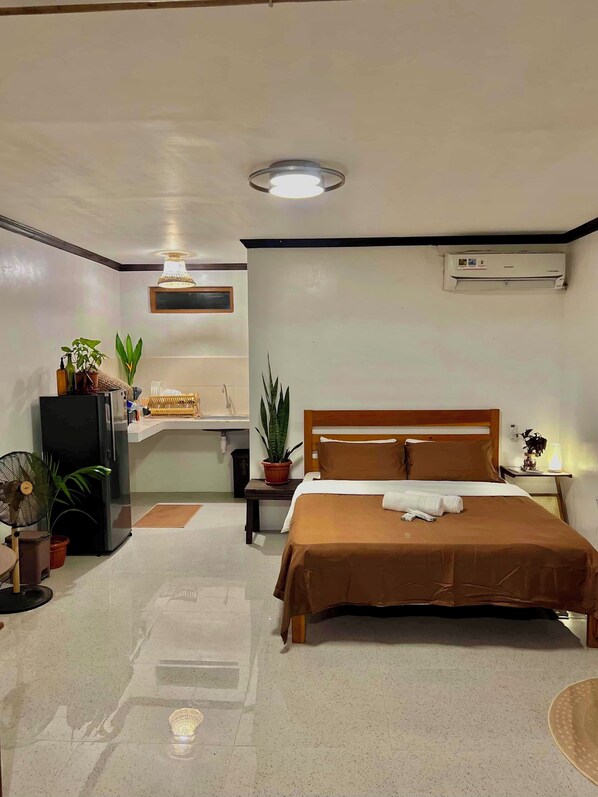 Un dormitorio con cama, mesita de noche, ventilador de techo y plantas en macetas. Incluye aire acondicionado de pared.