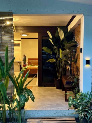 A modern interior with a wooden bench, potted plants, and a glass door leading to a room.