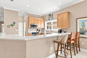 A kitchen with wooden cabinets, a microwave, a stove, and a large island with bar stools. - Krusty Krab | Sleeps 10 |  Bay Views Pet-Friendly (Gulf Shores)