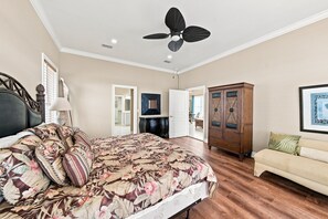Ein Schlafzimmer mit einem Bett, Deckenventilator, Schminktisch, einem Sessel und einem gerahmten Bild an der Wand.