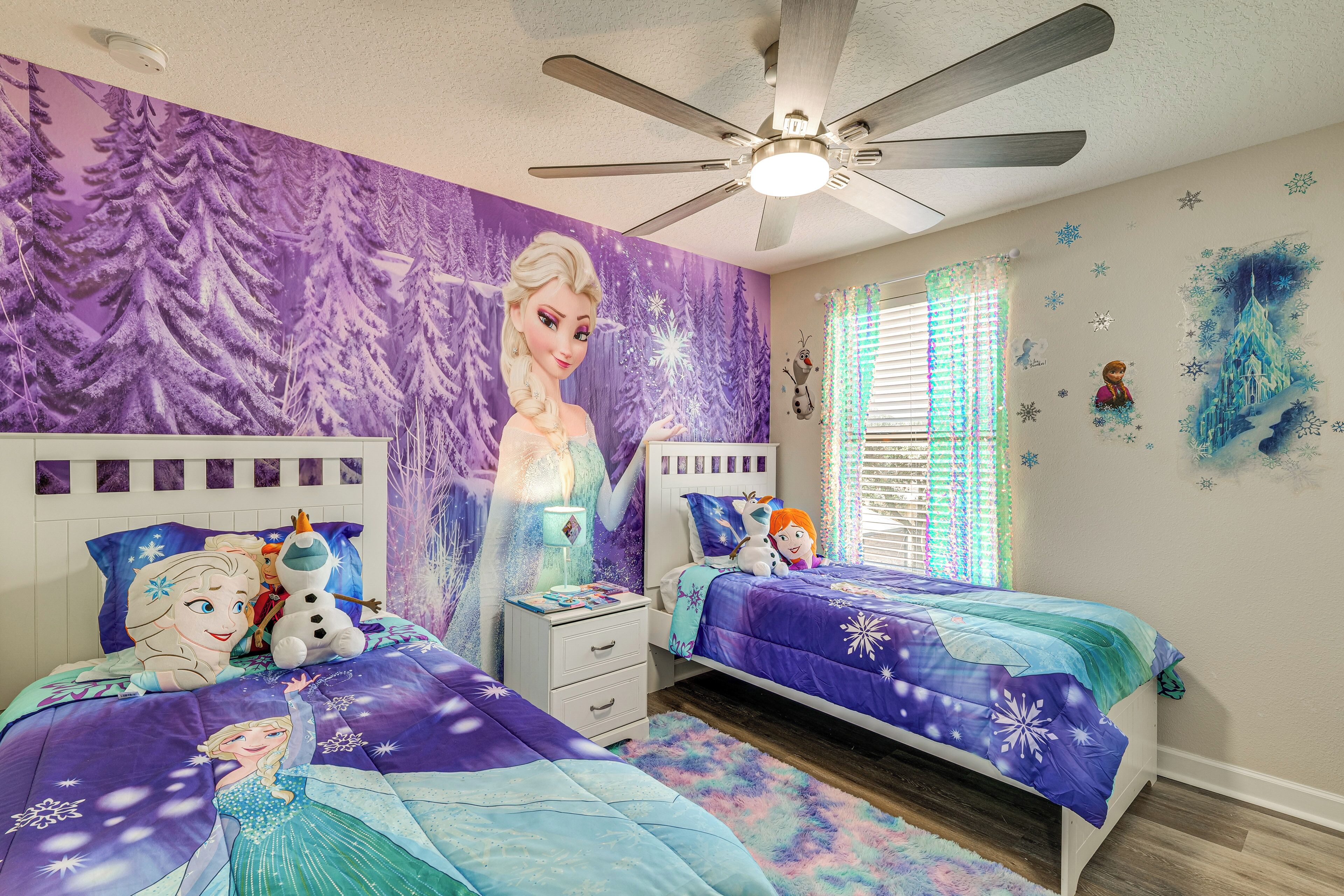 A bedroom with two beds, a ceiling fan, and a wall mural.
