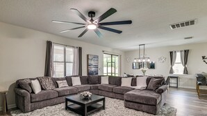 A living room with a sectional sofa, a coffee table, a ceiling fan, and a dining area with a table and chairs. - New Remodeled Championsgate Pool Home 5br/5ba (Davenport)