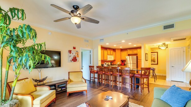 A living room with a sofa, armchair, coffee table, and a large plant. There is a dining area with chairs and a table, and a kitchen in the background. - Extended-stay Condo in Reunion Golf Resort (Kissimmee)