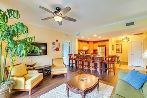 A living room with a sofa, armchair, coffee table, and a large plant. There is a dining area with chairs and a table, and a kitchen in the background. - Extended-stay Condo in Reunion Golf Resort (Kissimmee)