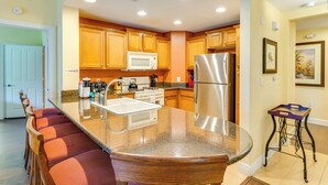 A kitchen with wooden cabinets, a stainless steel refrigerator, a microwave, and a granite countertop. - Extended-stay Condo in Reunion Golf Resort (Kissimmee)