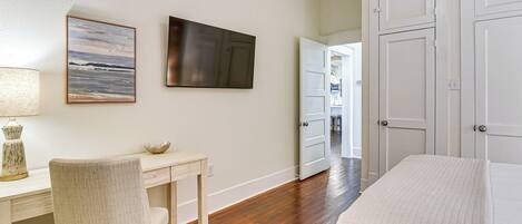 A bedroom with a bed, a desk with a chair, a painting, and a door leading to another room.