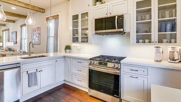A modern kitchen with white cabinetry, a stainless steel stove, a microwave, and a coffee maker. - 1 Block to Beach: Fire Pit, Outdoor Kitchen, Bikes (Galveston)