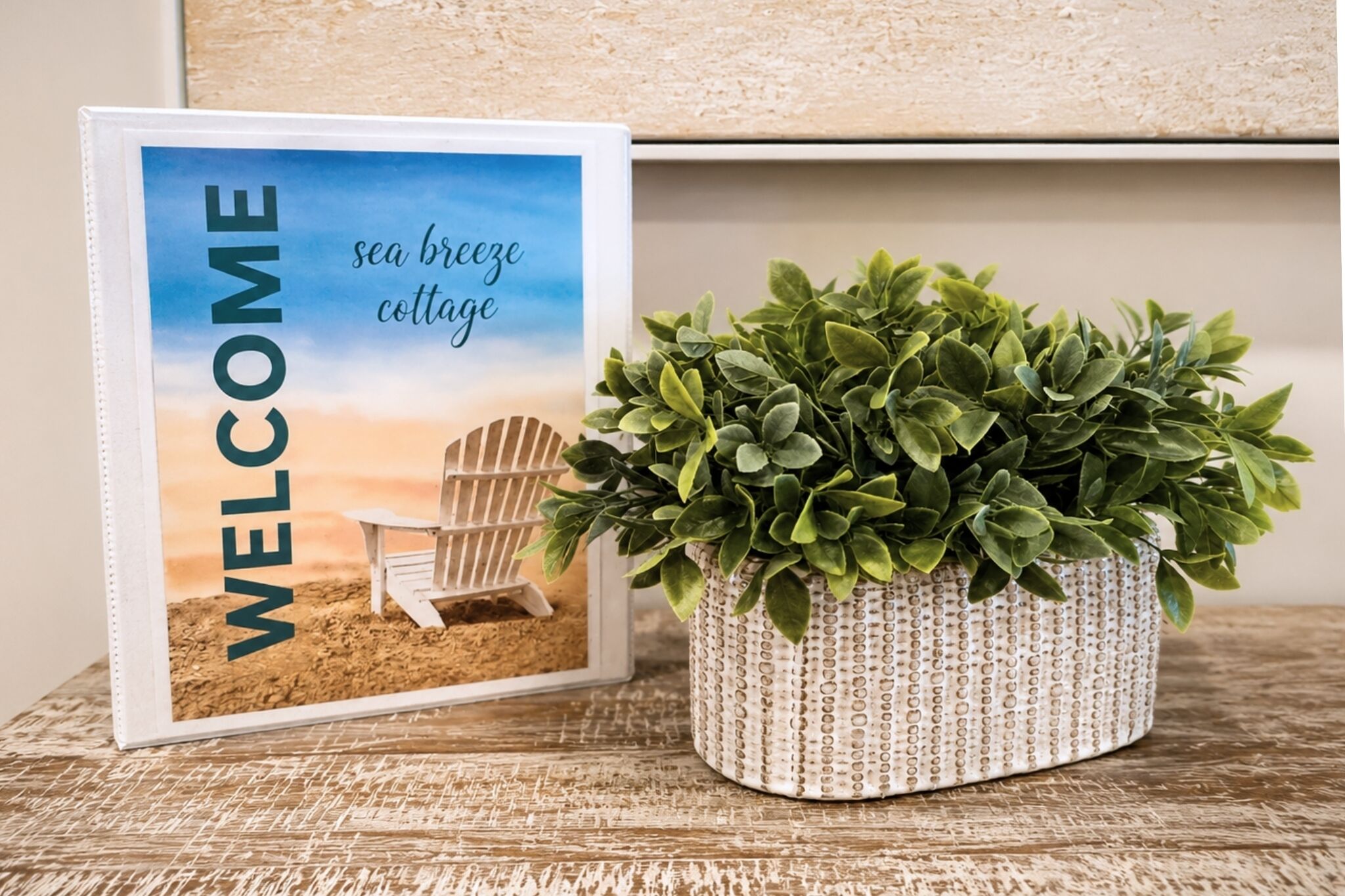 Un letrero de bienvenida enmarcado con una escena de playa y una planta en maceta.