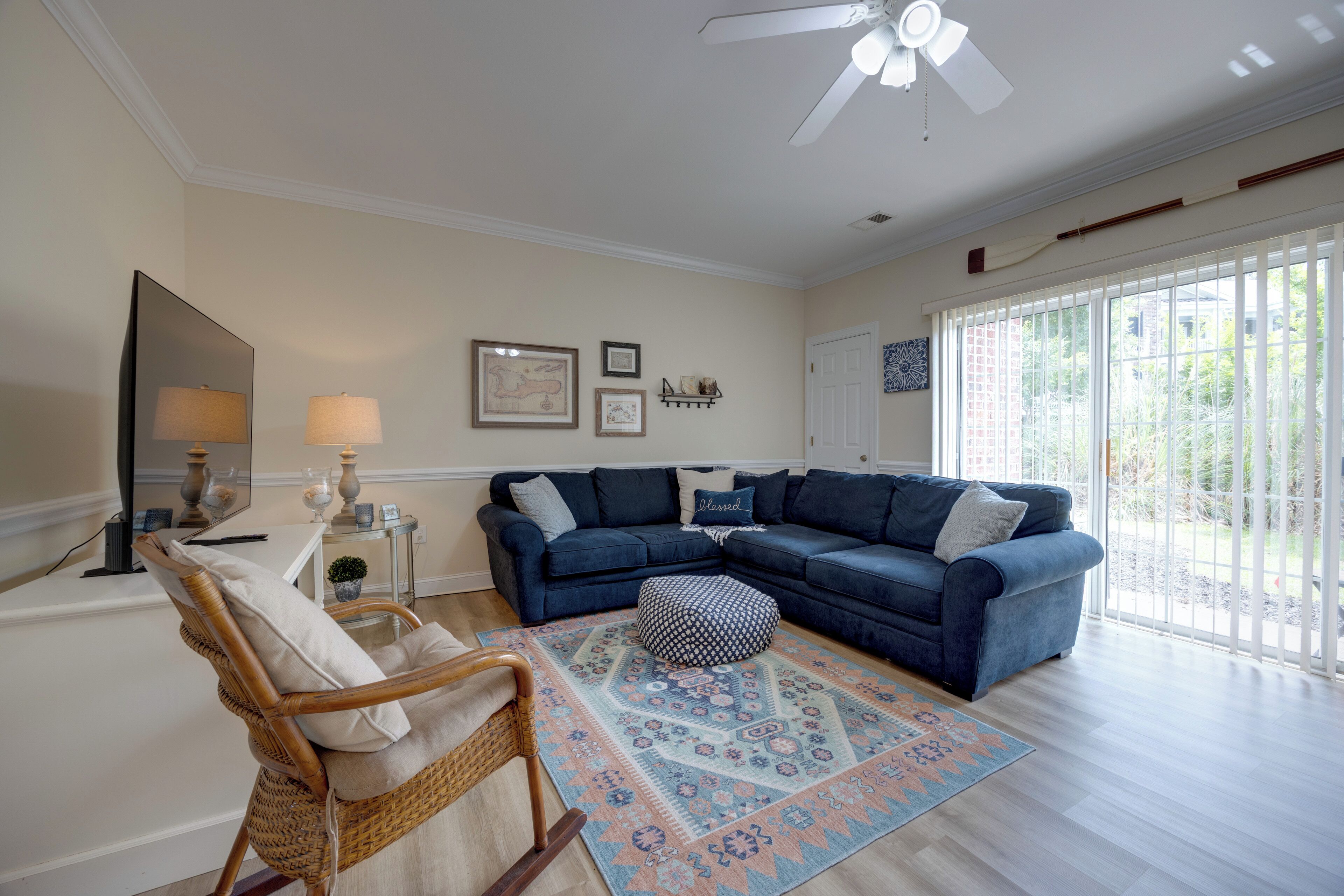Una sala de estar con un sofá modular, un sillón de ratán, un tapete estampado y un ventilador de techo.
