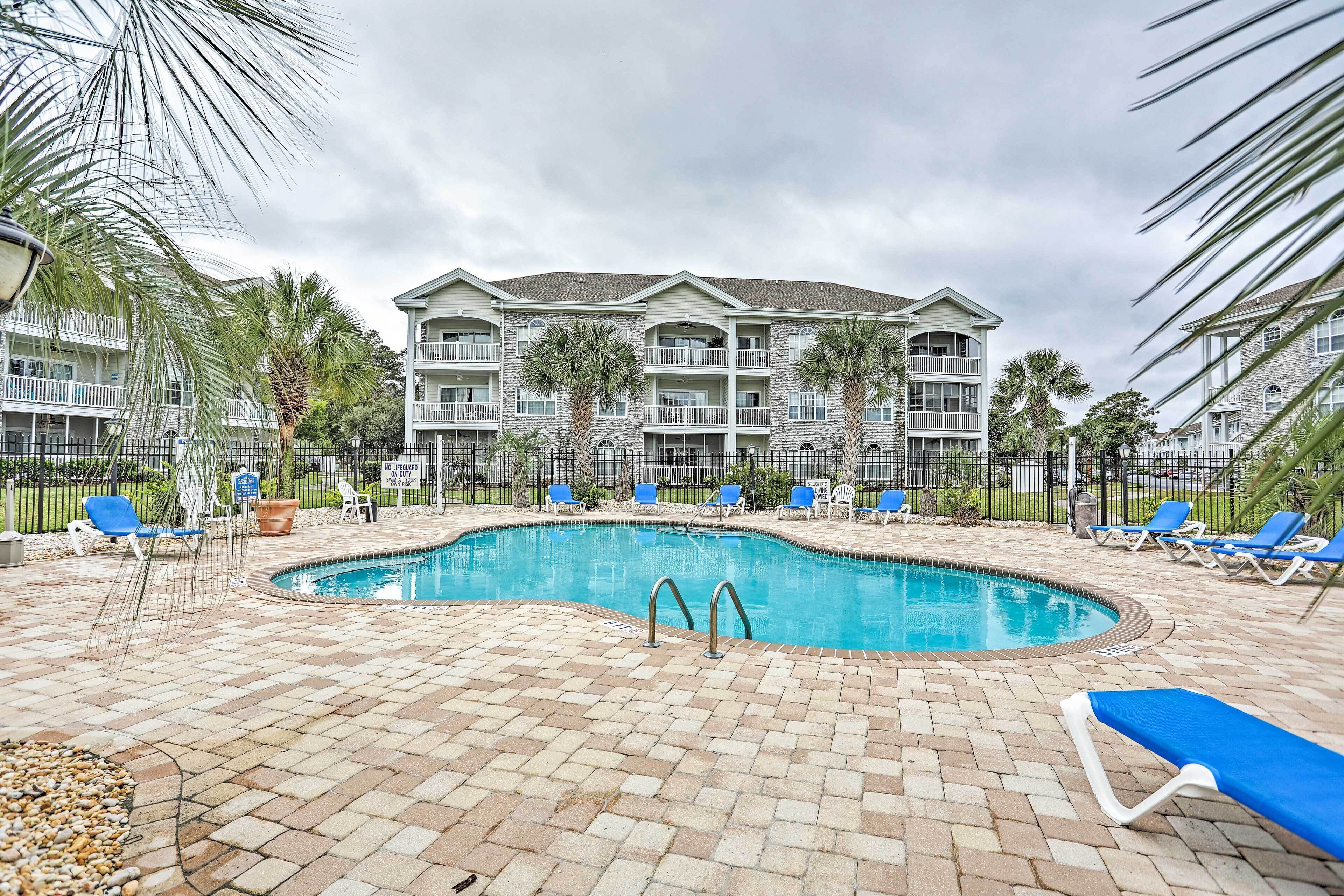 A swimming pool with lounge chairs and palm trees, surrounded by a brick patio.