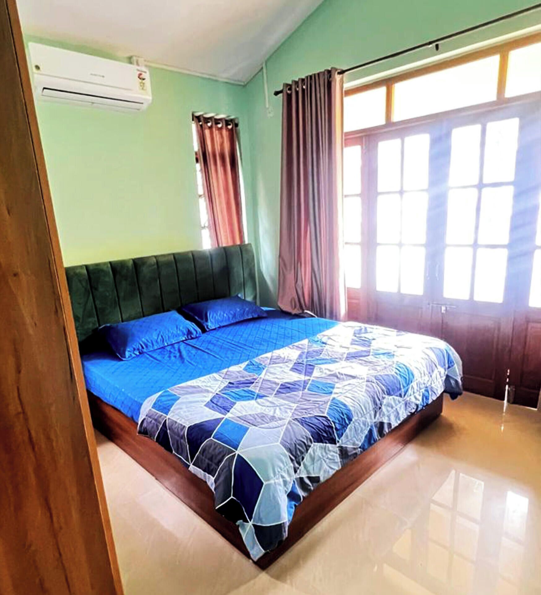 A bedroom with a bed, a window with curtains, and an air conditioning unit.
