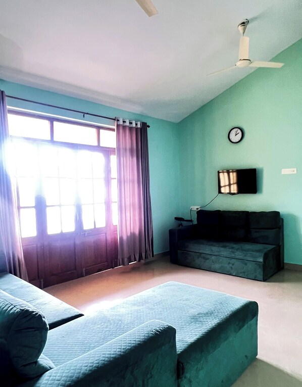 A room with a bed, a sofa, a TV, and a clock on the wall. - 3 Balconies 1-BHK 900sq. ft Near Benaulim Beach Goa Private Entry & Parking WiFi (Benaulim)