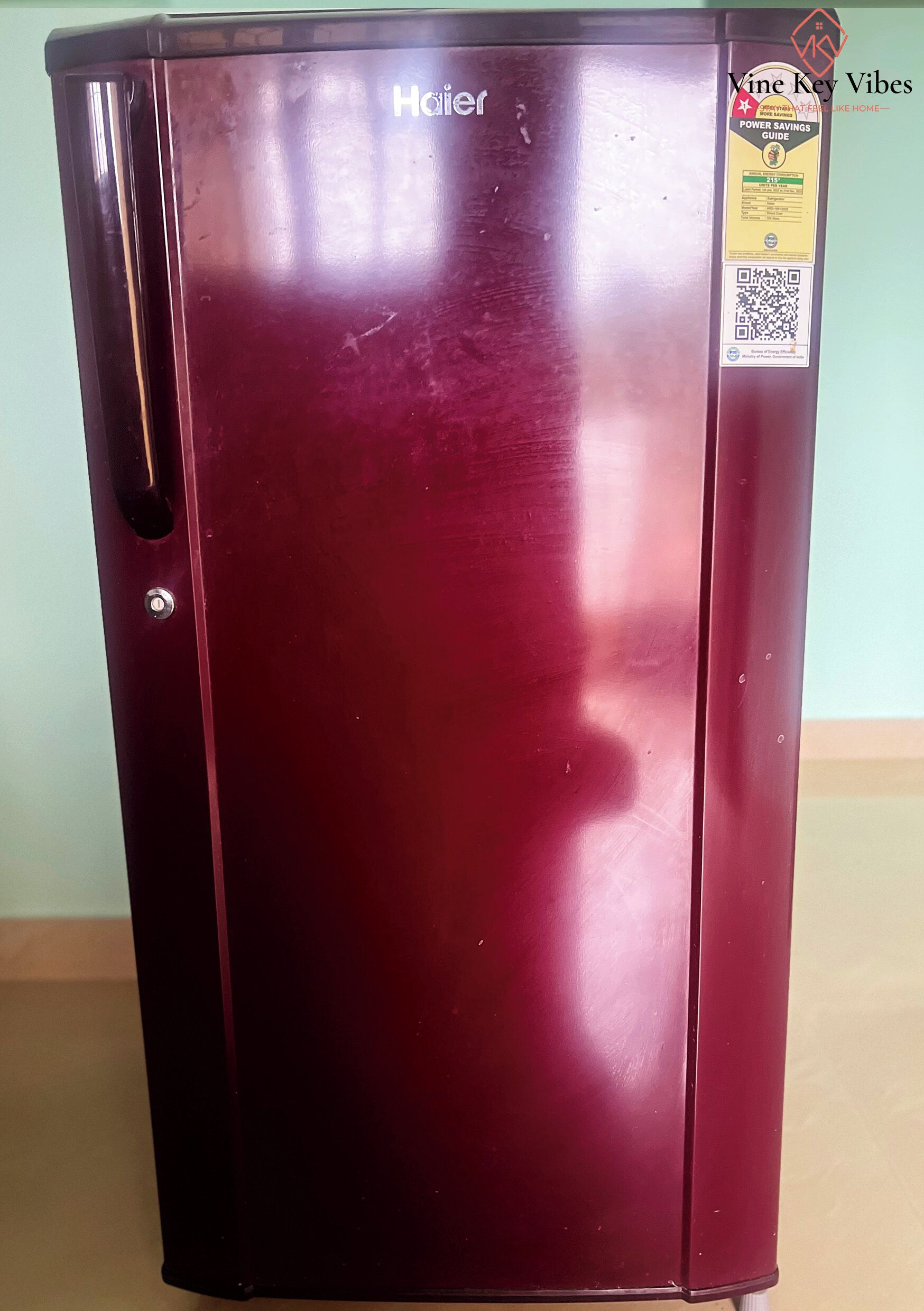 Un réfrigérateur Haier de couleur bordeaux, muni d’un autocollant indiquant les mesures à prendre pour économiser l’énergie.