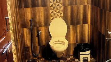 A compact bathroom with a toilet, shower, and a small trash bin.