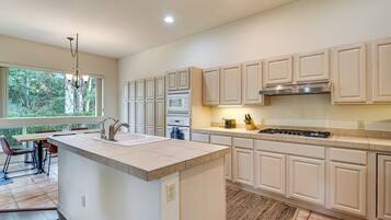 A modern kitchen with white cabinetry, a central island, and a dining area with a view of trees.