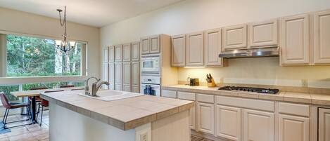 A modern kitchen with white cabinetry, a central island, and a dining area with a view of trees.
