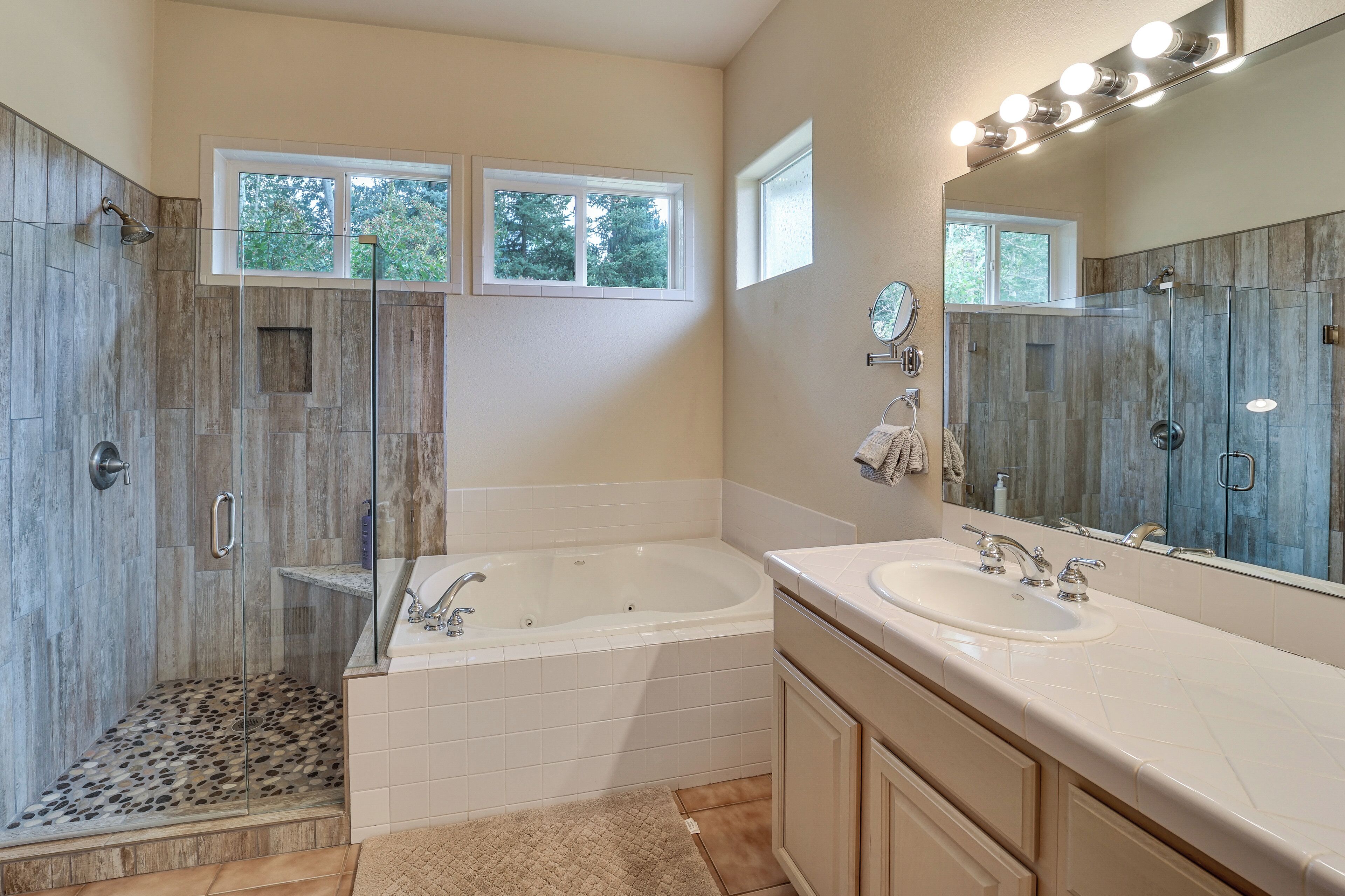 A bathroom with a walk-in shower, a bathtub, a vanity with a sink, and a large mirror with lights.
