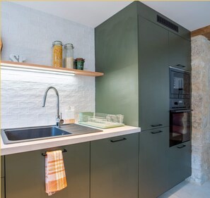 A kitchen with a built-in sink, a wooden shelf with jars, a dish rack, and a built-in oven. - La Halte du Vigneron I T2 I Vongnes (Vongnes)