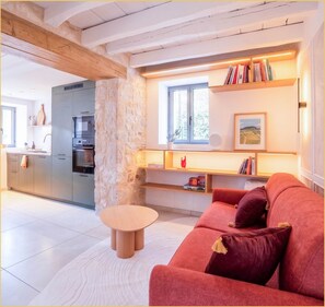 A modern living room with a red sofa, a round wooden coffee table, and a stone accent wall. - La Halte du Vigneron I T2 I Vongnes (Vongnes)