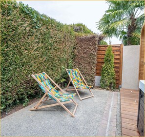 Two wooden lounge chairs with colorful fabric, a gravel patio, a wooden fence, and a dense hedge. - La Halte du Vigneron I T2 I Vongnes (Vongnes)