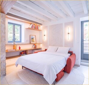 A modern bedroom with a bed, built-in shelving, bedside lamps, and a view through a window. - La Halte du Vigneron I T2 I Vongnes (Vongnes)