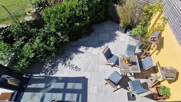 Eine Terrasse im Freien mit Tisch und Stühlen, umgeben von Grünpflanzen und einem Holzboden.