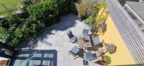 Un espace extérieur aménagé en terrasse, avec une table et des chaises, entouré de verdure et doté d’une plateforme en bois.