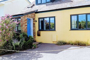 A yellow building with a blue door, a stone wall, and a garden with pink flowers. - Petrichor - coastal retreat in Bantham South Devon (Bantham)