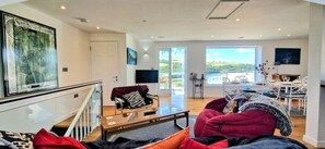 A spacious living area with a sofa, a coffee table, and a television. There is a balcony with a view of the outdoors.