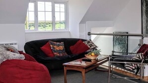 Ein Loft-Zimmer mit schwarzem Sofa, roten Kissen, einem kleinen Holztisch und einem Glasgeländer.