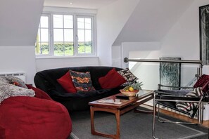 Ein Loft-Zimmer mit schwarzem Sofa, roten Kissen, einem kleinen Holztisch und einem Glasgeländer.
