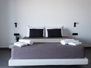 Une chambre moderne avec un grand lit, deux oreillers noirs et du linge de lit blanc. On y trouve deux tables de chevet avec des lampes.