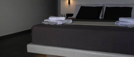 A modern bedroom with a bed, bedside tables, and a wall-mounted light fixture.