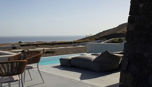 A poolside area with lounge chairs and a stone wall. - Lithora Suites (Oia)