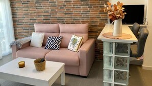 Ein Wohnzimmer mit Backsteinwand, einem rosafarbenen Sofa, einem weißen Couchtisch und einem Fernseher auf einem Lowboard.