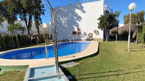 Ein Schwimmbecken mit gefliestem Sonnendeck, umgeben von Gras und Bäumen.