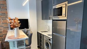 Eine kompakte Küche mit Mikrowelle, Kühlschrank, Waschmaschine und einem kleinen Spülbecken.