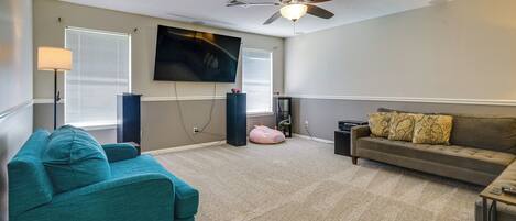 Una sala de estar con un sofá azul turquesa, un sofá marrón, un ventilador de techo, un televisor de pantalla plana y un sillón de peluche.