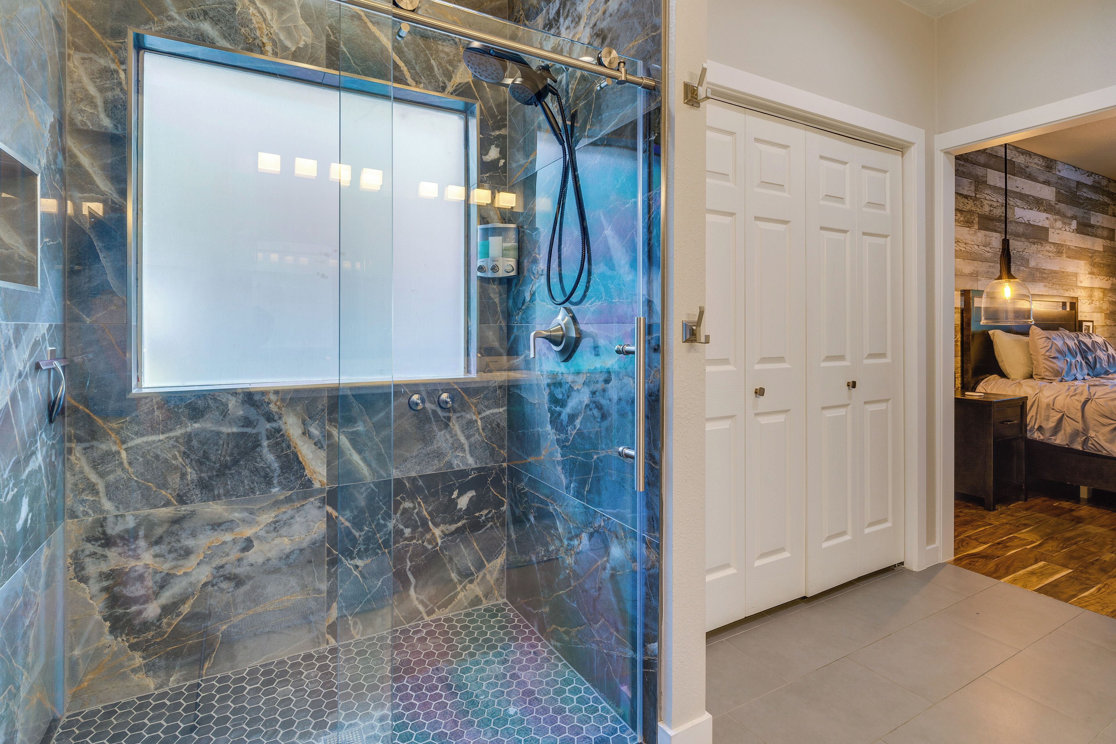 A bathroom with a glass-enclosed shower, marble walls, and a white door.