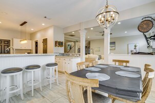 Una cocina moderna con armarios blancos, una isla central, taburetes de bar y una mesa de comedor con individuales.
