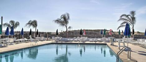 A pool area with lounge chairs and umbrellas, surrounded by a stone wall and palm trees.