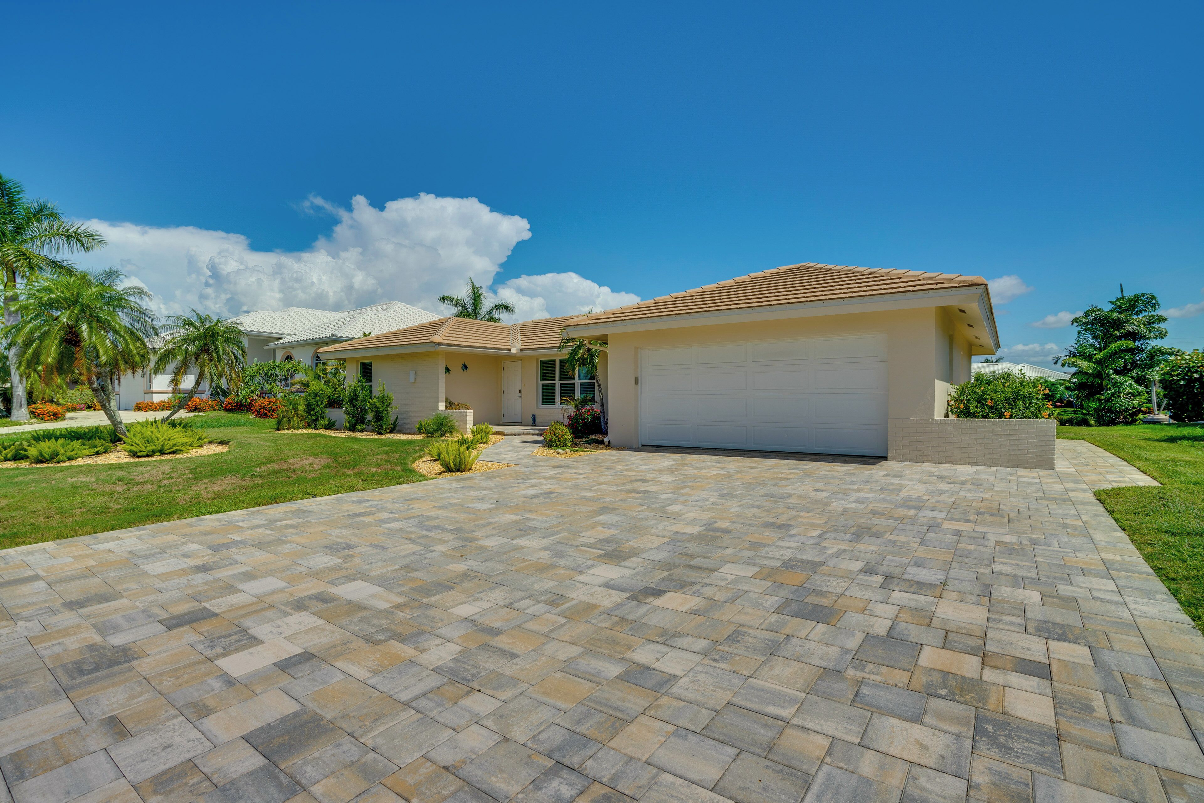 A two-story house with a garage, a paved driveway, and a well-maintained lawn with palm trees.