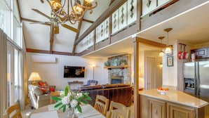 Comedor con mesa, sillas, una araña, chimenea y cocina con refrigerador.