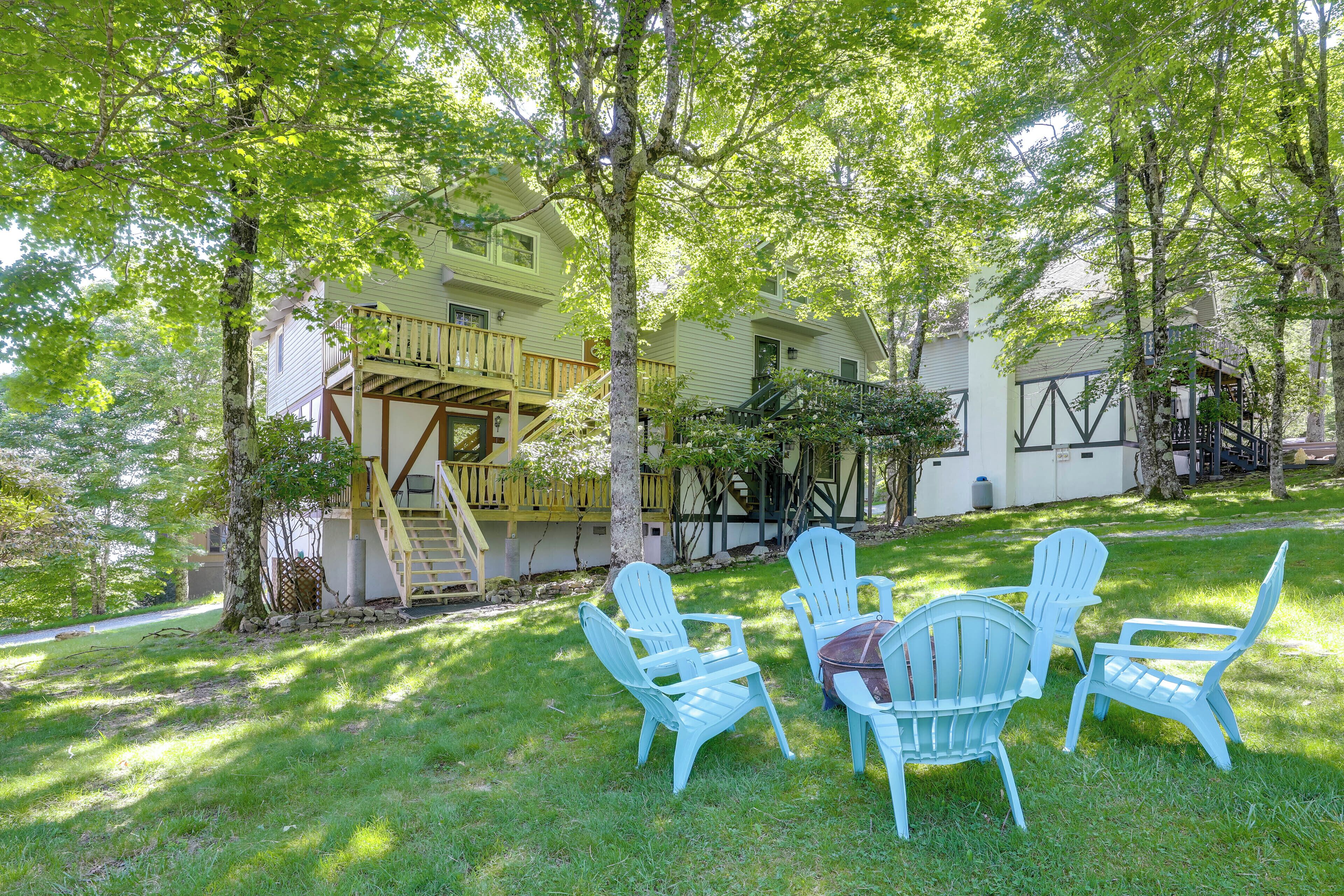 A two-story building with a balcony, surrounded by trees and a grassy area with Adirondack chairs.