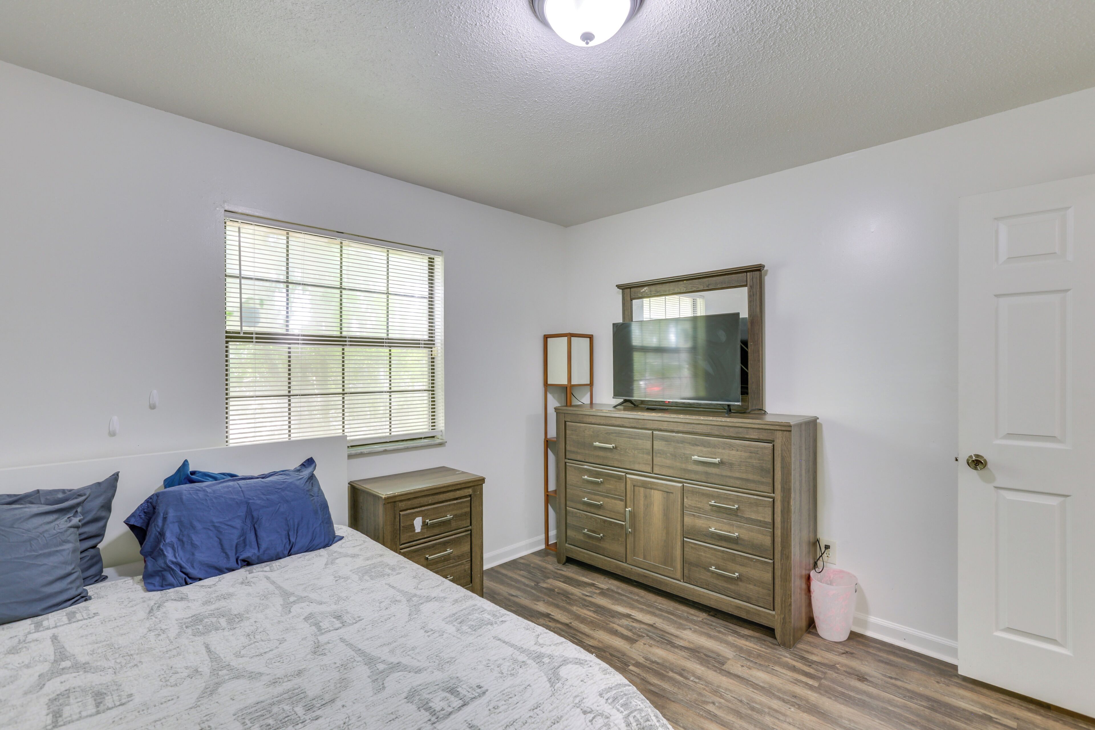 A bedroom with a bed, dresser, mirror, and window.