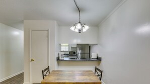 Comedor con mesa de madera y sillas negras, cocina con electrodomésticos de acero inoxidable y una puerta blanca.