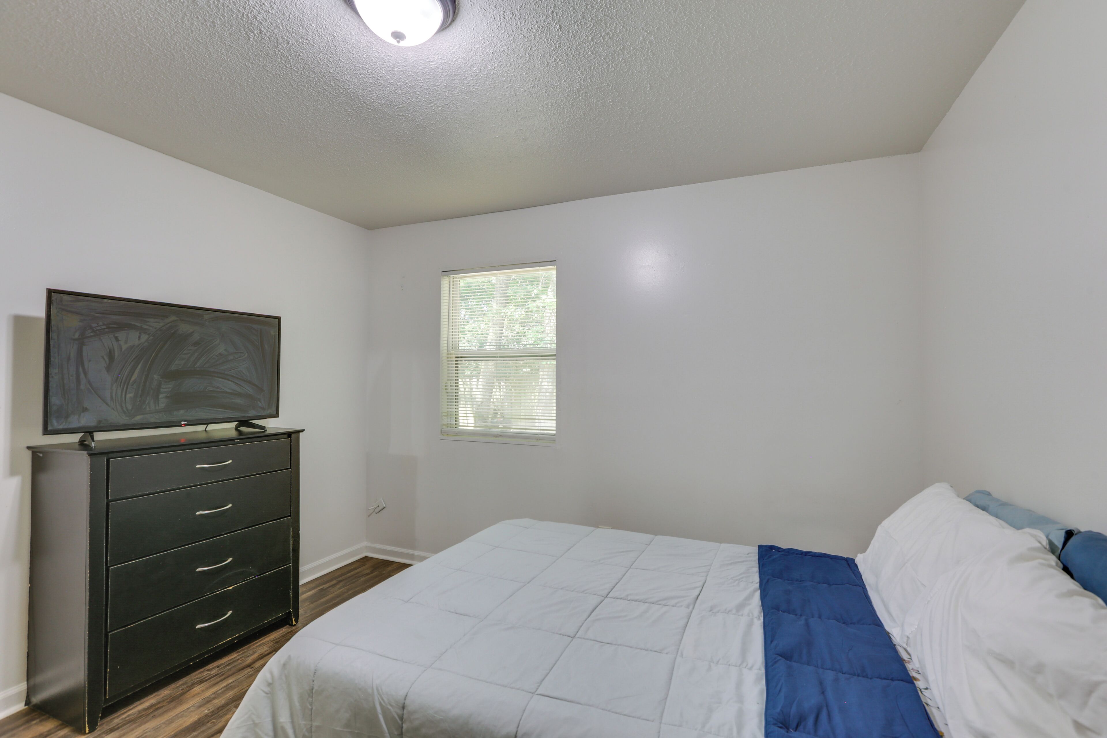 Un dormitorio con cama, cómoda, televisor y ventana.