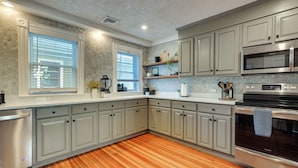 Una cocina con gabinetes grises, lavavajillas de acero inoxidable, horno negro y piso de madera.